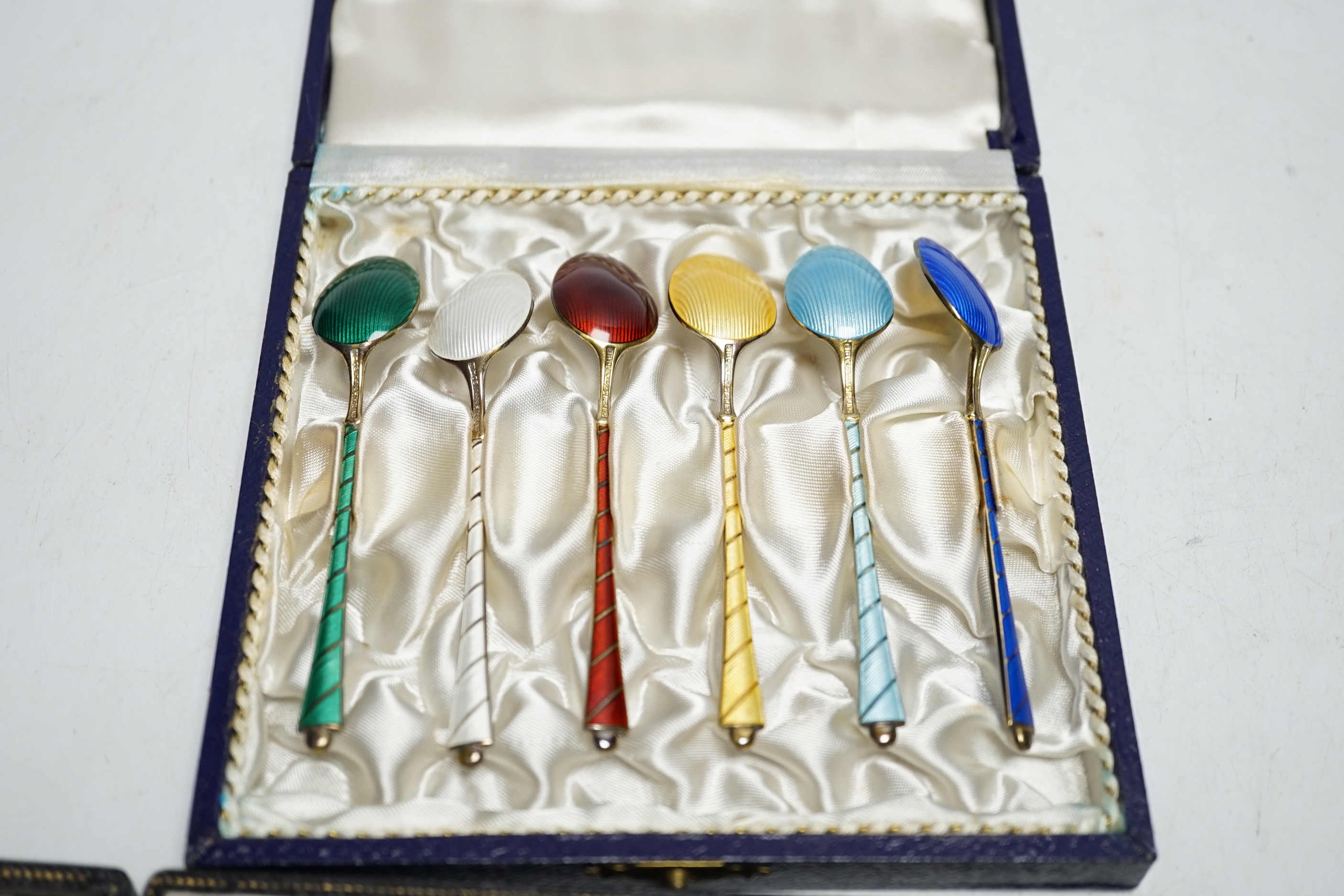 A cased set of six Danish gilt sterling and polychrome enamelled coffee spoons and a cased set of eight enamelled white metal cocktail sticks, stamped 'silver', the terminals decorated with the floral emblem of the count